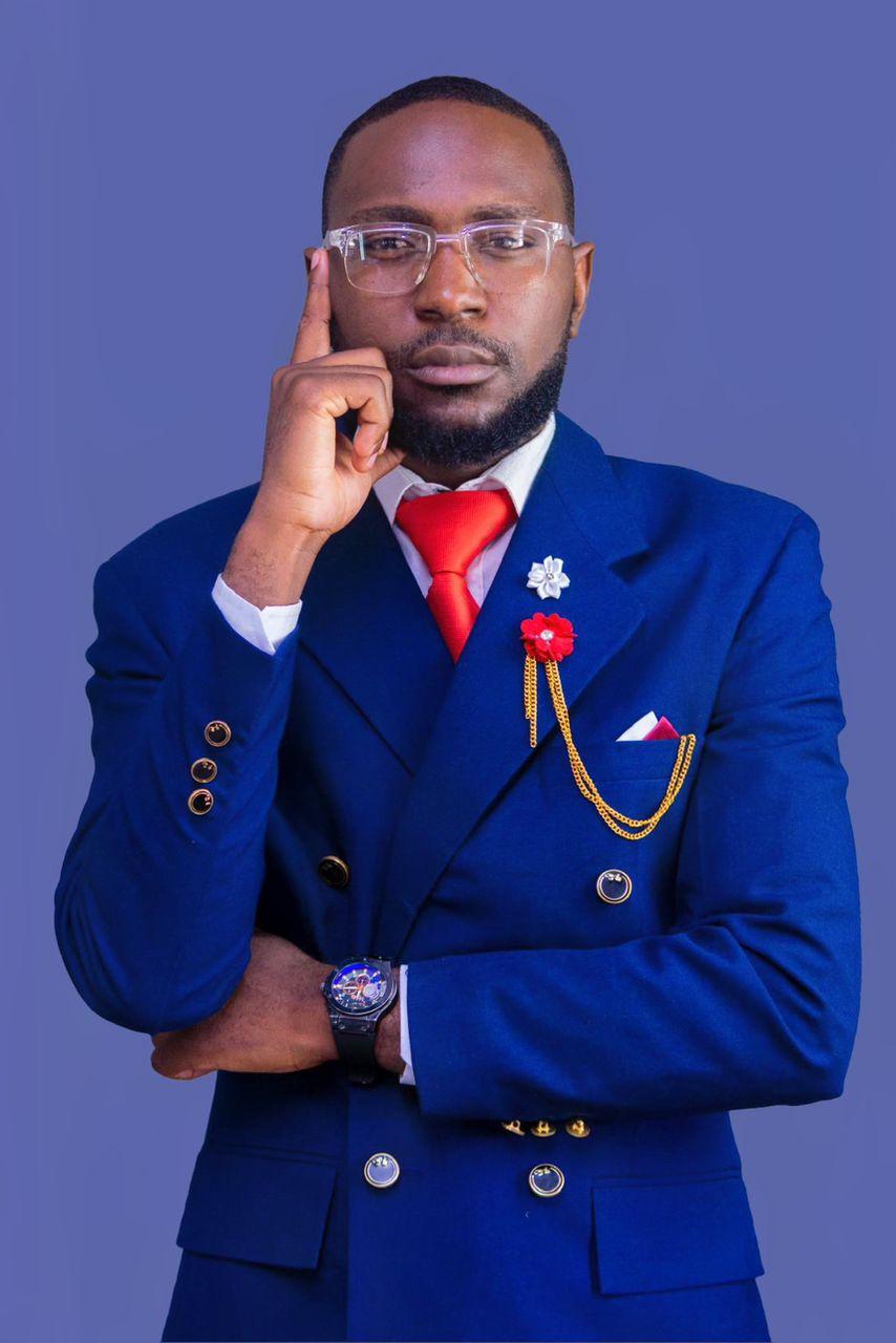Patrick Mwewa in a royal blue suit and red tie, hand raised to his temple