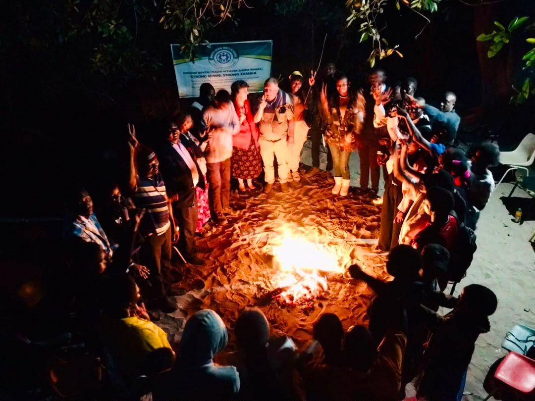 A crowd around a bonfire at night in Mwandi, hands raised
