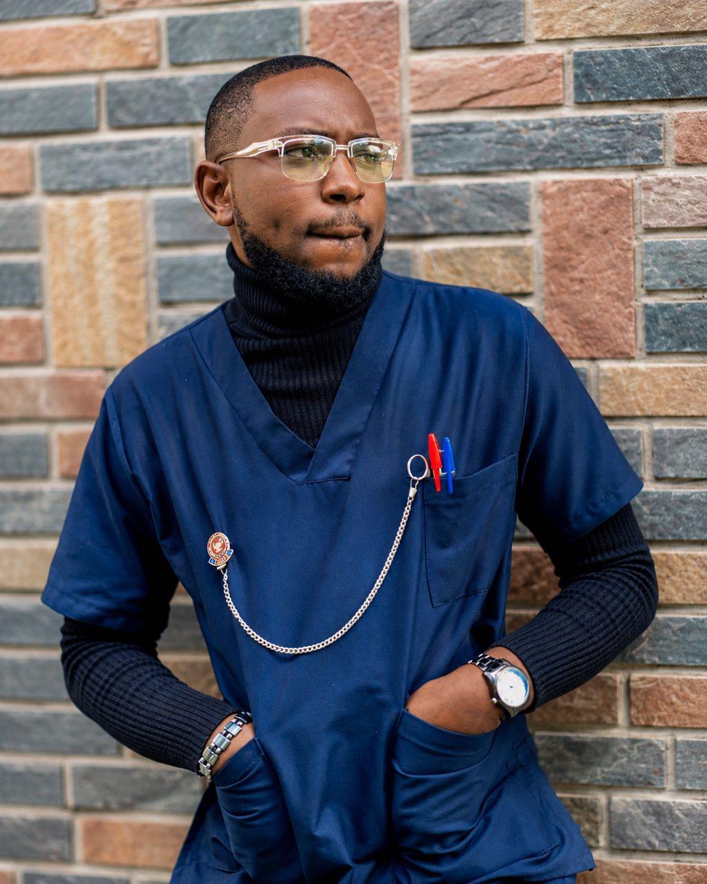 Patrick Mwewa in navy nursing scrubs against a stone wall